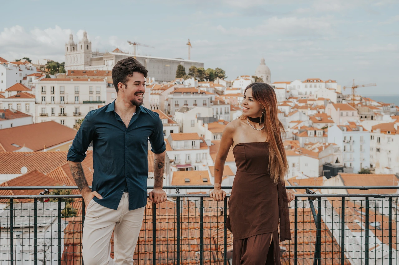 A shared smile above the rooftops | Lisbon engagement photoshoot The couple sharing a smile with the city skyline behind them at Portas do Sol during their engagement photoshoot in Lisbon.