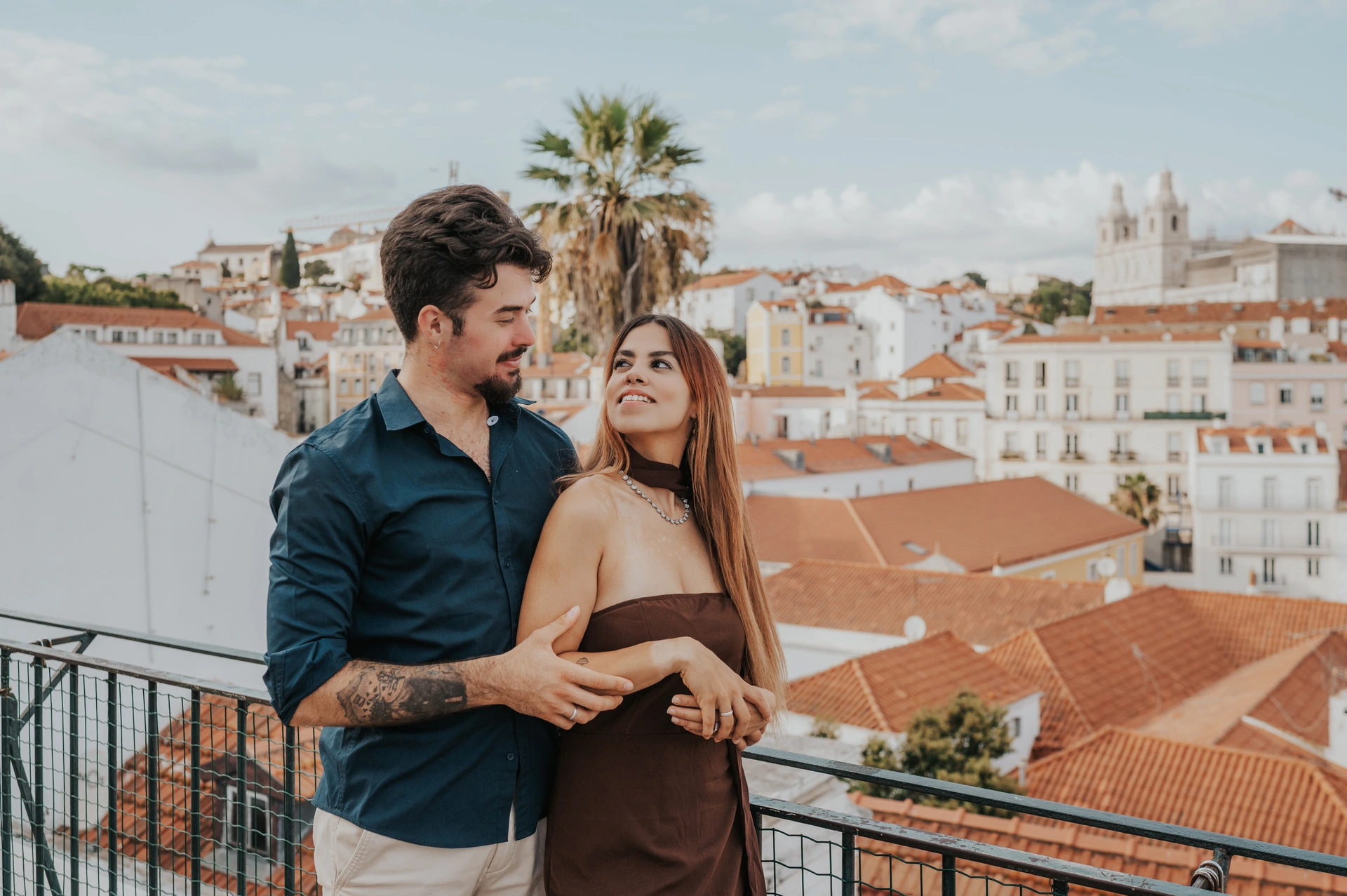 The couple smiling at one another over her shoulder at Portas do Sol during their engagement photoshoot in Lisbon.