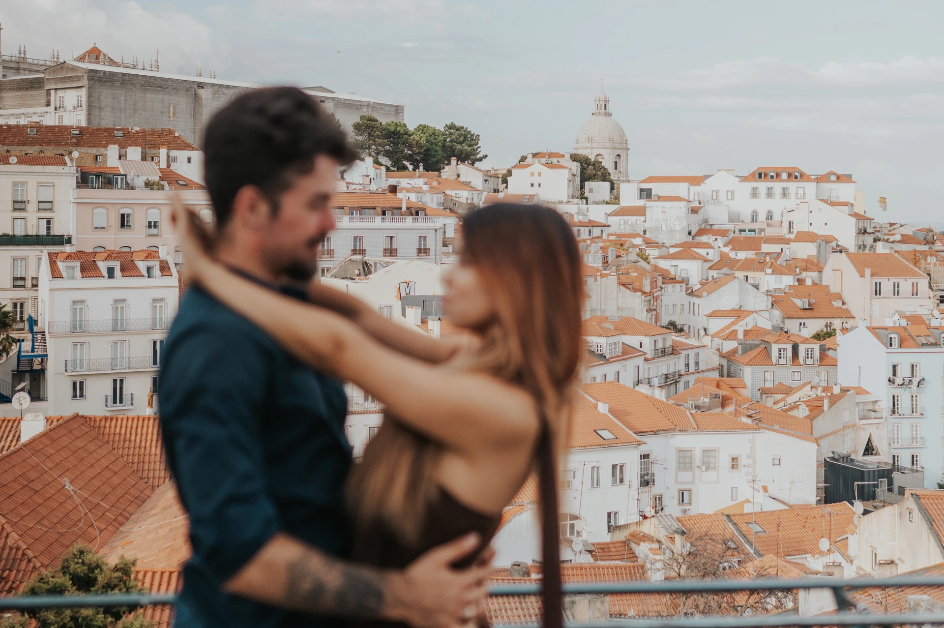 A softly focused embrace with sharp rooftops in the background at Portas do Sol during their engagement photoshoot in Lisbon.