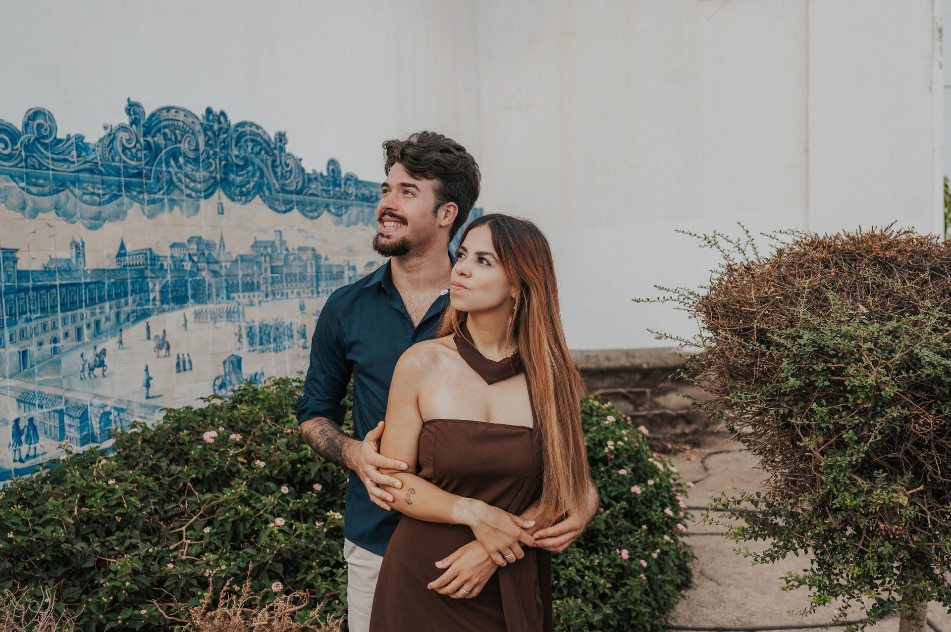 The couple embracing and looking upwards beside the blue tiled wall at Santa Luzia during their engagement photoshoot in Lisbon.