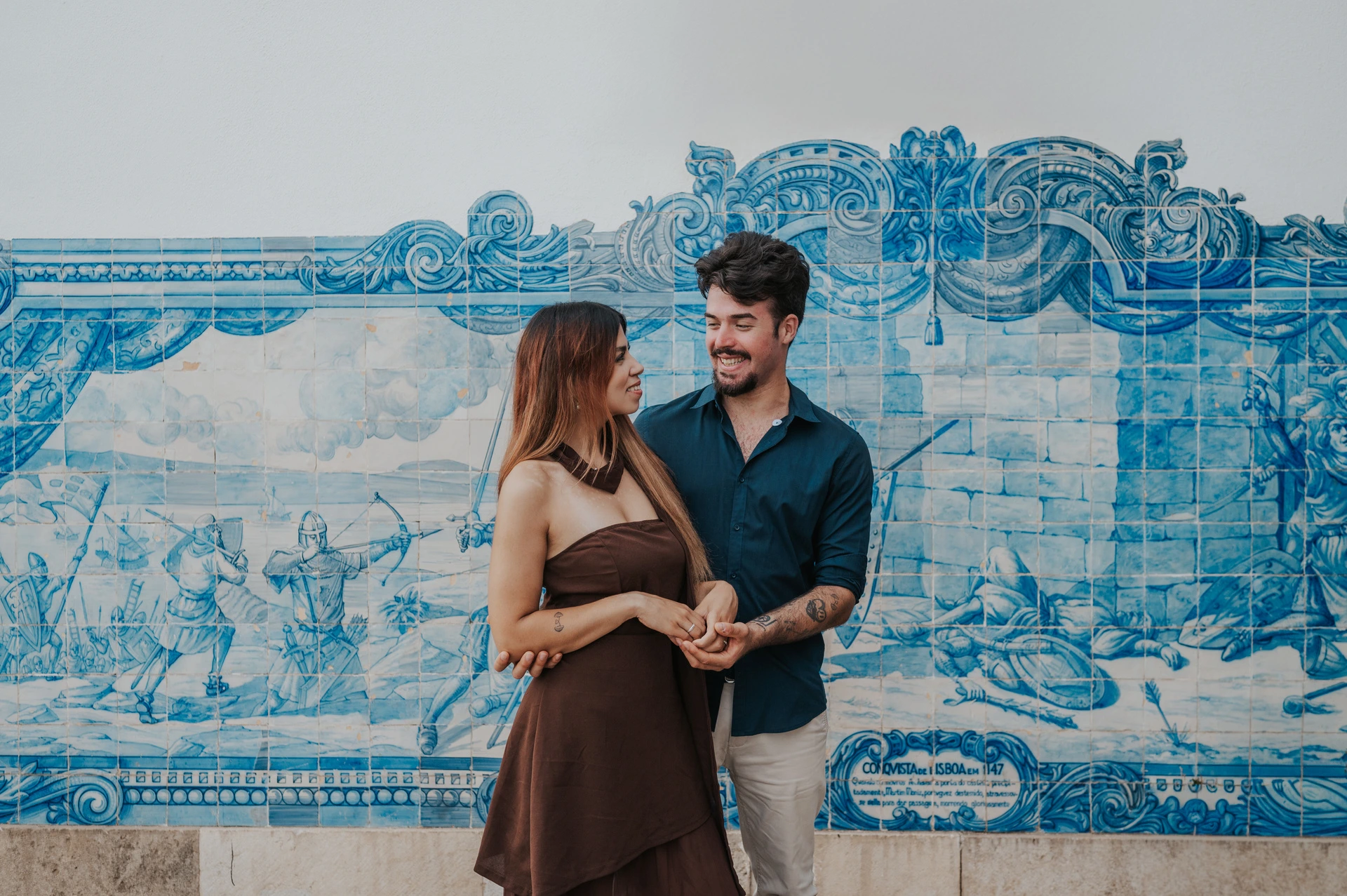 The couple looking at each other in front of blue-and-white tiles at Santa Luzia during their engagement photoshoot in Lisbon.