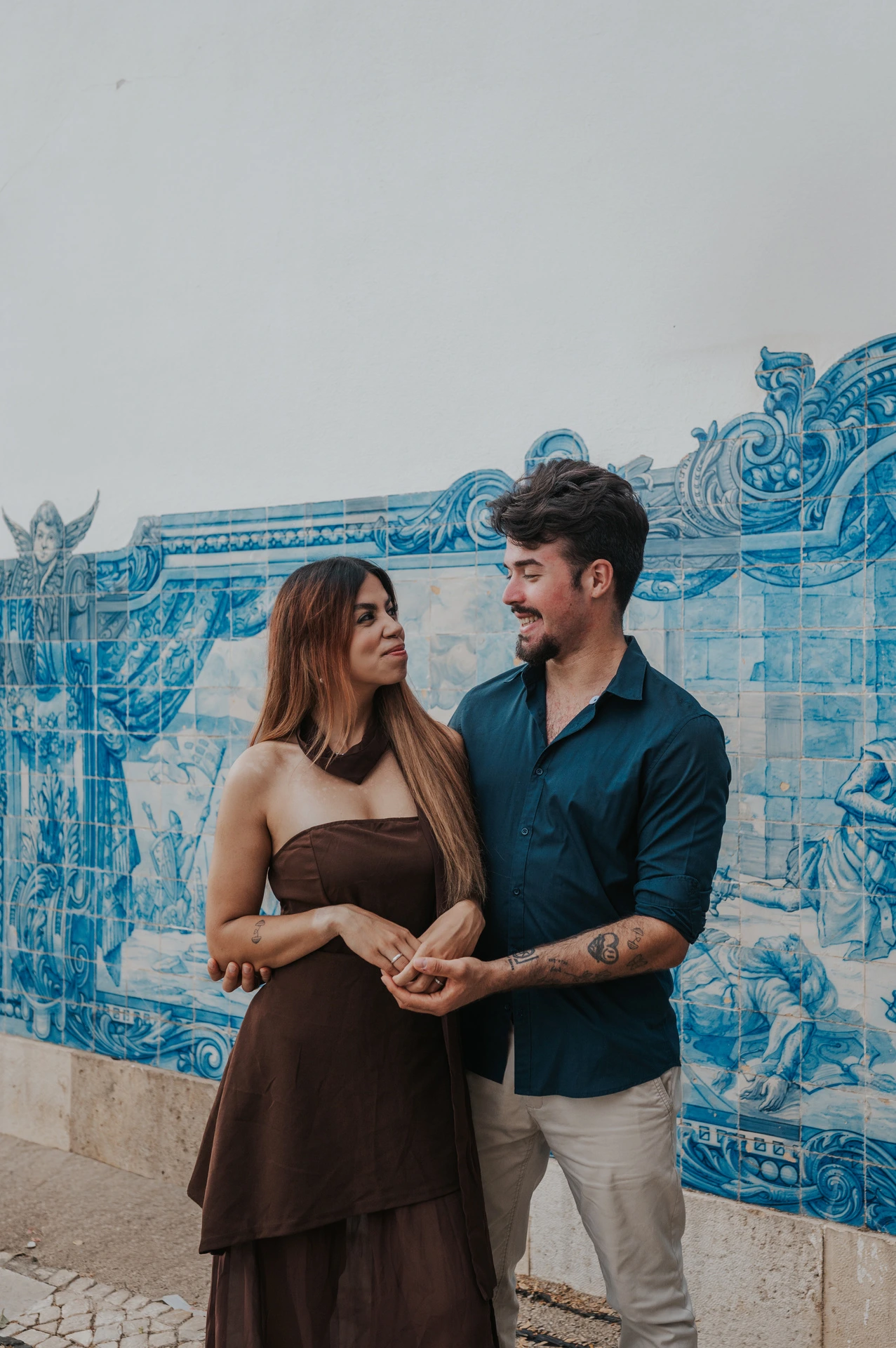 A vertical portrait of the couple holding hands beside the blue-and-white tile wall at Santa Luzia during their engagement photoshoot in Lisbon.