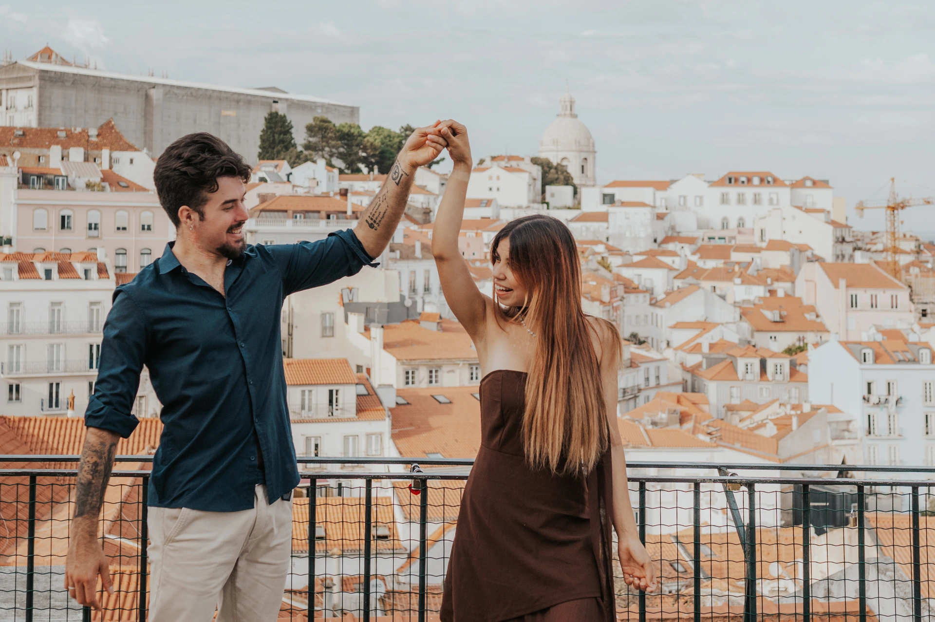 A twirl above the Portas do Sol rooftops | Lisbon engagement photoshoot The woman turning beneath her partner’s raised hand above the rooftops at Portas do Sol during their engagement photoshoot in Lisbon.