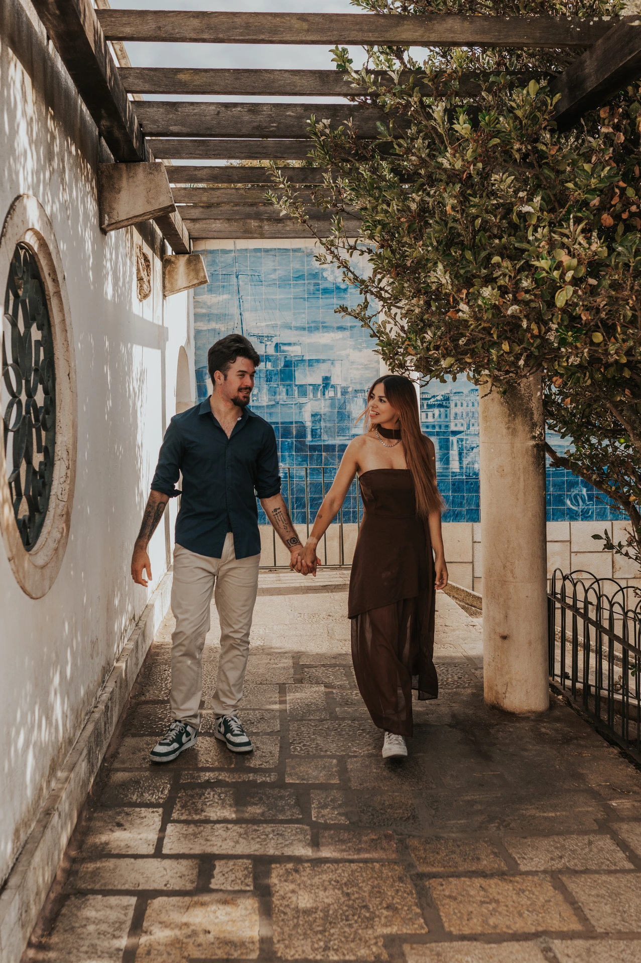 The couple walking hand in hand beneath the wooden pergola at Santa Luzia during their engagement photoshoot in Lisbon.