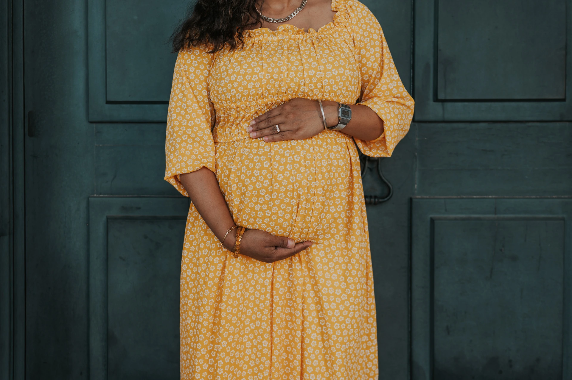 A close detail of the expectant mother’s hands resting on her yellow dress over her belly during their family and maternity photoshoot in Lisbon.