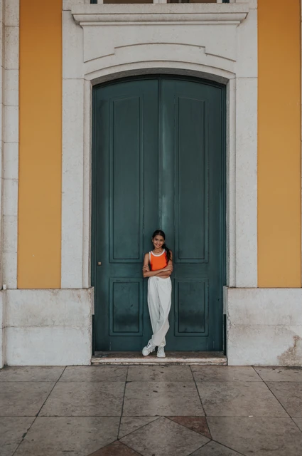 A portrait at the green doorway | Lisbon family and maternity photoshoot The daughter standing in front of a tall green door framed by the square’s yellow walls during their family and maternity photoshoot in Lisbon.