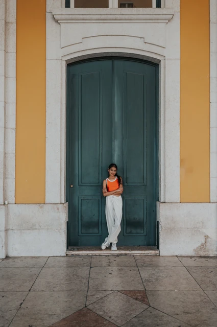 A portrait at the green doorway | Lisbon family and maternity photoshoot The daughter standing in front of a tall green door framed by the square’s yellow walls during their family and maternity photoshoot in Lisbon.