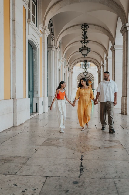 A family walk beneath the arcade | Lisbon family and maternity photoshoot The parents and daughter walking hand in hand beneath the stone arcade during their family and maternity photoshoot in Lisbon.