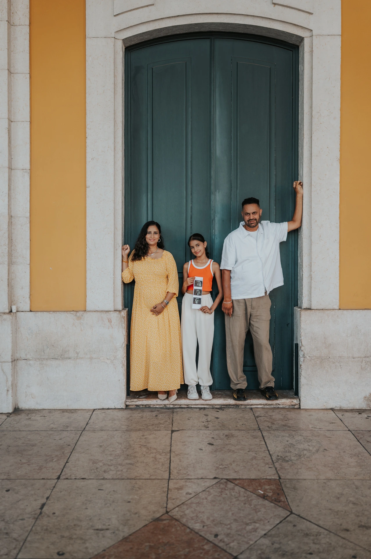 The family standing side by side against the green doorway and yellow wall during their family and maternity photoshoot in Lisbon.