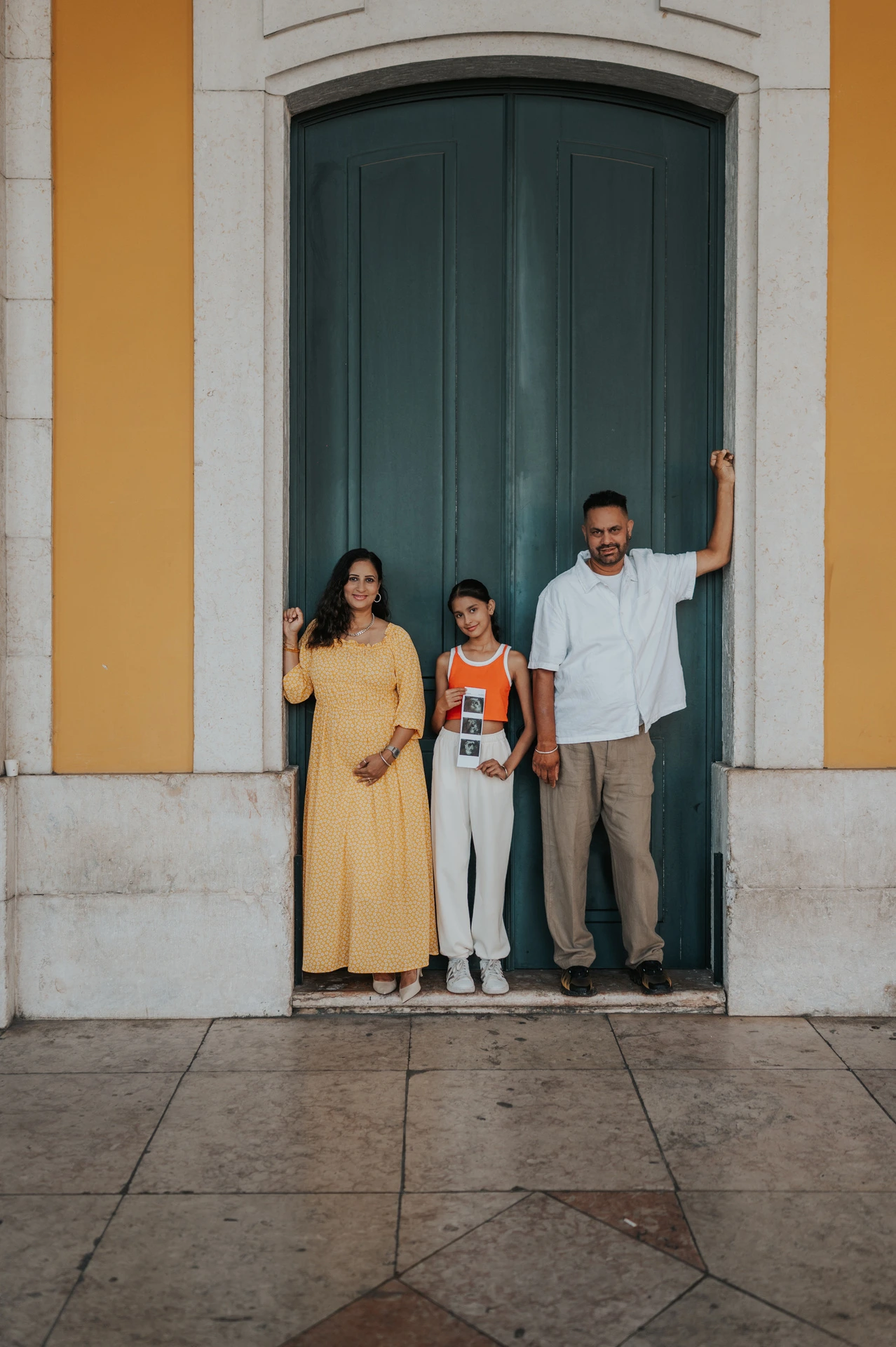 The family standing side by side against the green doorway and yellow wall during their family and maternity photoshoot in Lisbon.