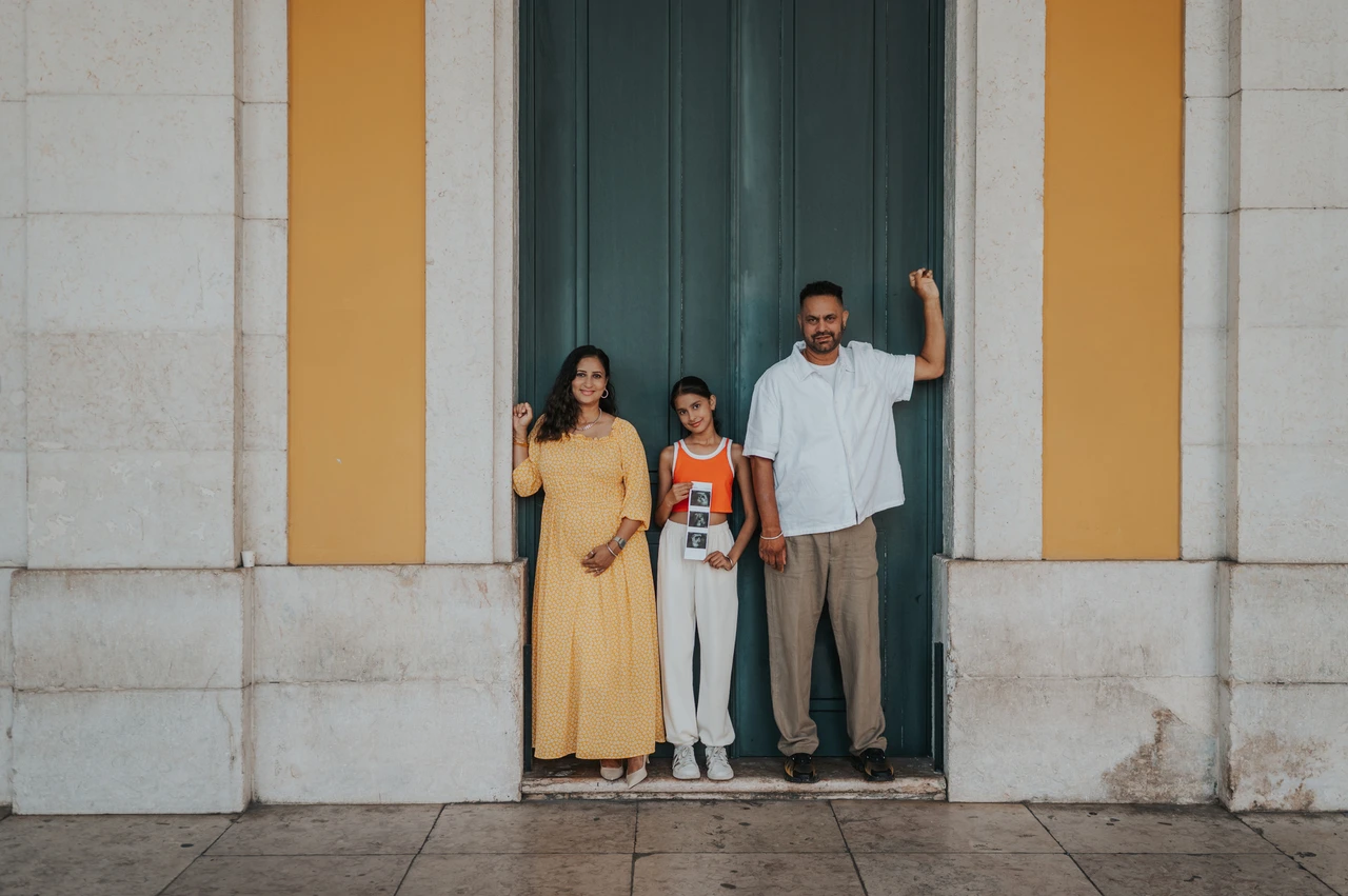 Together against the square’s yellow façade | Lisbon family and maternity photoshoot The family standing side by side against the green doorway and yellow wall during their family and maternity photoshoot in Lisbon.