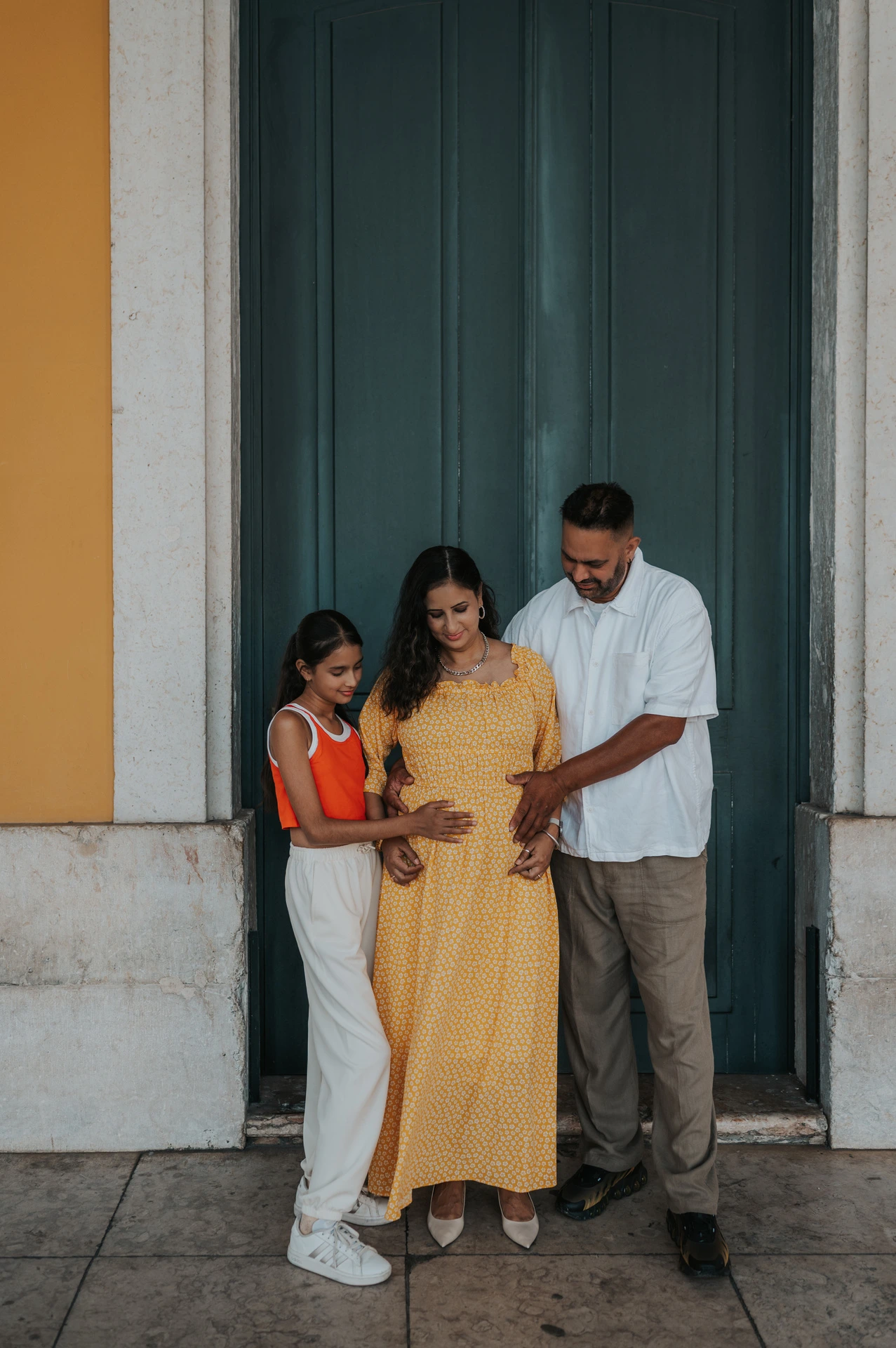 The parents and daughter looking down with their hands resting on the mother’s belly during their family and maternity photoshoot in Lisbon.