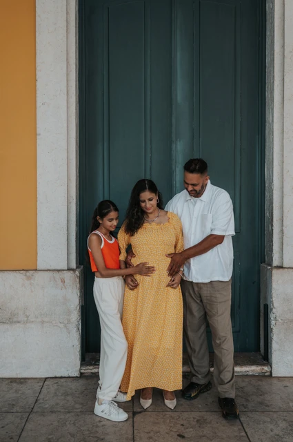 A family moment around the baby bump | Lisbon family and maternity photoshoot The parents and daughter looking down with their hands resting on the mother’s belly during their family and maternity photoshoot in Lisbon.