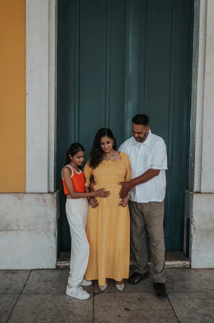 A family moment around the baby bump | Lisbon family and maternity photoshoot The parents and daughter looking down with their hands resting on the mother’s belly during their family and maternity photoshoot in Lisbon.