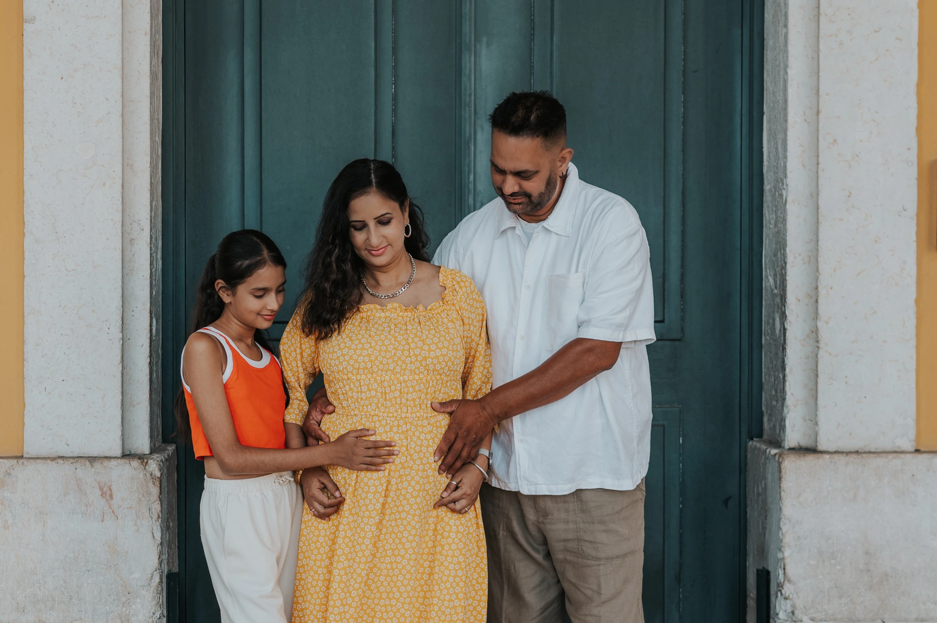 The parents and daughter looking down with their hands resting on the mother’s belly during their family and maternity photoshoot in Lisbon.