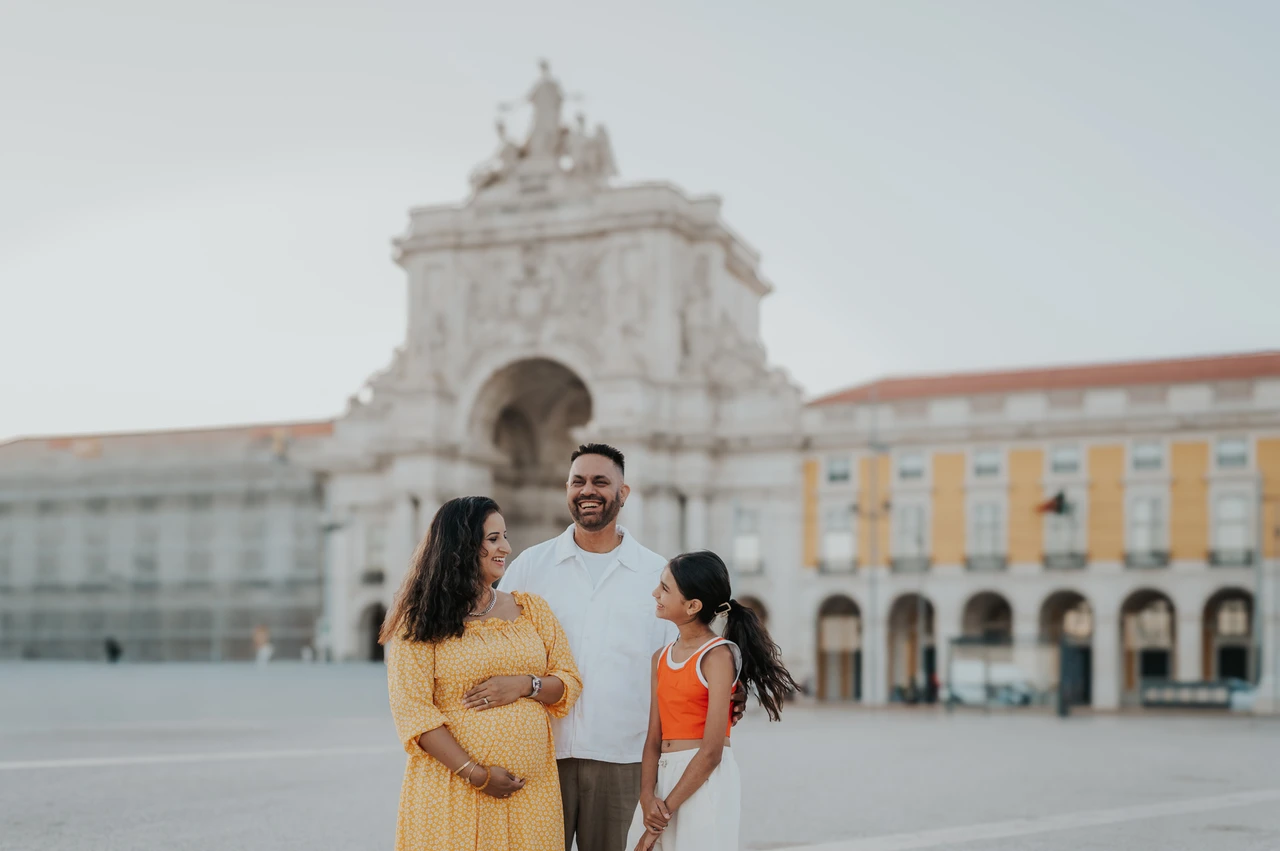 A close family portrait in the square | Lisbon family and maternity photoshoot The family standing close together and smiling in front of Praça do Comércio’s arch during their family and maternity photoshoot in Lisbon.