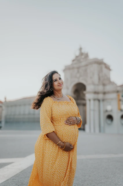 A maternity portrait in the open square | Lisbon family and maternity photoshoot The expectant mother holding her belly with the square’s arch behind her during their family and maternity photoshoot in Lisbon.