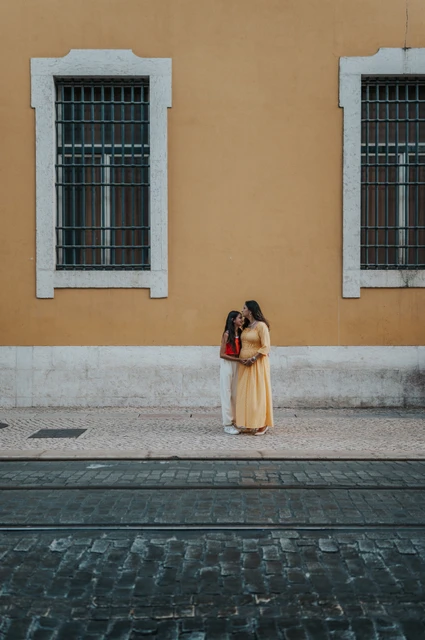 A mother-and-daughter portrait by the yellow wall | Lisbon family and maternity photoshoot The daughter leaning close to her mother beside the yellow wall during their family and maternity photoshoot in Lisbon.