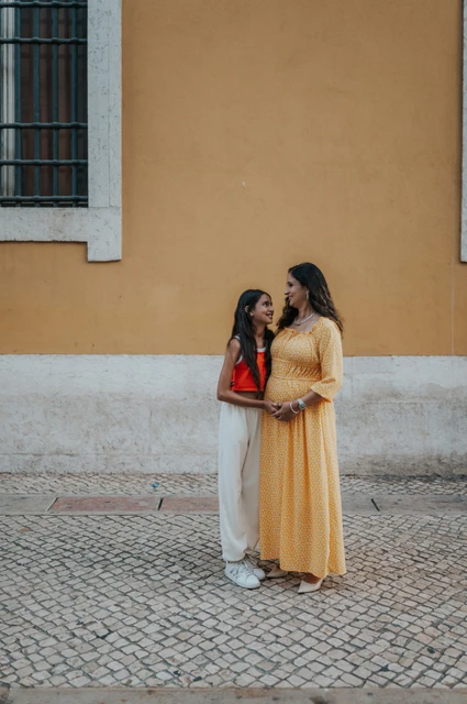 A mother-and-daughter portrait by the yellow wall | Lisbon family and maternity photoshoot The daughter leaning close to her mother beside the yellow wall during their family and maternity photoshoot in Lisbon.