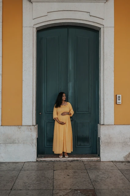 A maternity portrait at the green door | Lisbon family and maternity photoshoot The expectant mother holding her belly in front of the tall green door at Praça do Comércio during their family and maternity photoshoot in Lisbon.