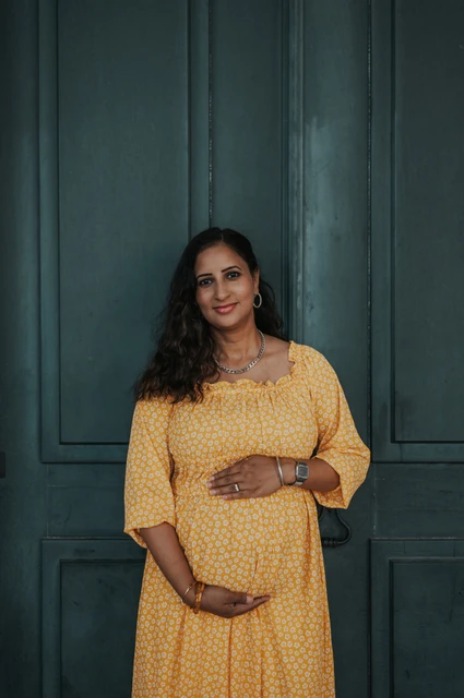 A maternity portrait at the green door | Lisbon family and maternity photoshoot The expectant mother holding her belly in front of the tall green door at Praça do Comércio during their family and maternity photoshoot in Lisbon.