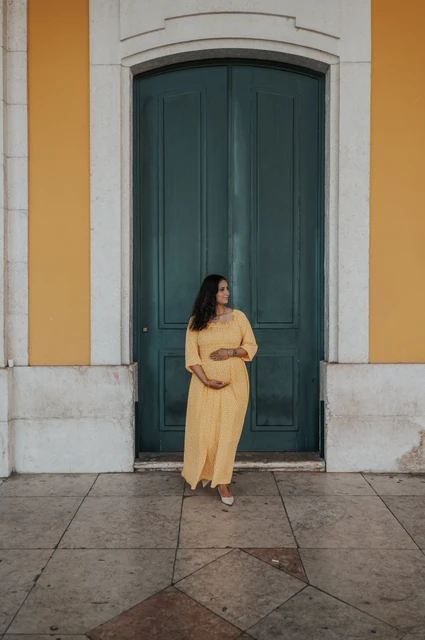 A maternity portrait at the green door | Lisbon family and maternity photoshoot The expectant mother holding her belly in front of the tall green door at Praça do Comércio during their family and maternity photoshoot in Lisbon.