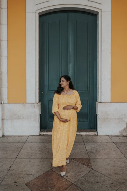A maternity portrait at the green door | Lisbon family and maternity photoshoot The expectant mother holding her belly in front of the tall green door at Praça do Comércio during their family and maternity photoshoot in Lisbon.