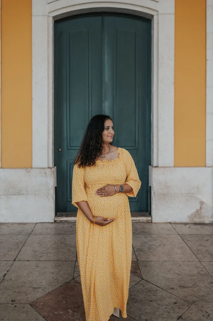 A maternity portrait at the green door | Lisbon family and maternity photoshoot The expectant mother holding her belly in front of the tall green door at Praça do Comércio during their family and maternity photoshoot in Lisbon.