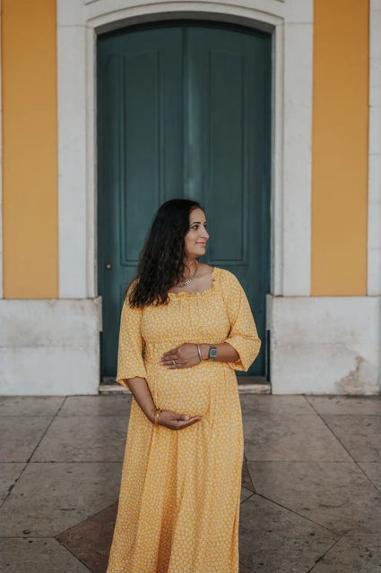 A maternity portrait at the green door | Lisbon family and maternity photoshoot The expectant mother holding her belly in front of the tall green door at Praça do Comércio during their family and maternity photoshoot in Lisbon.