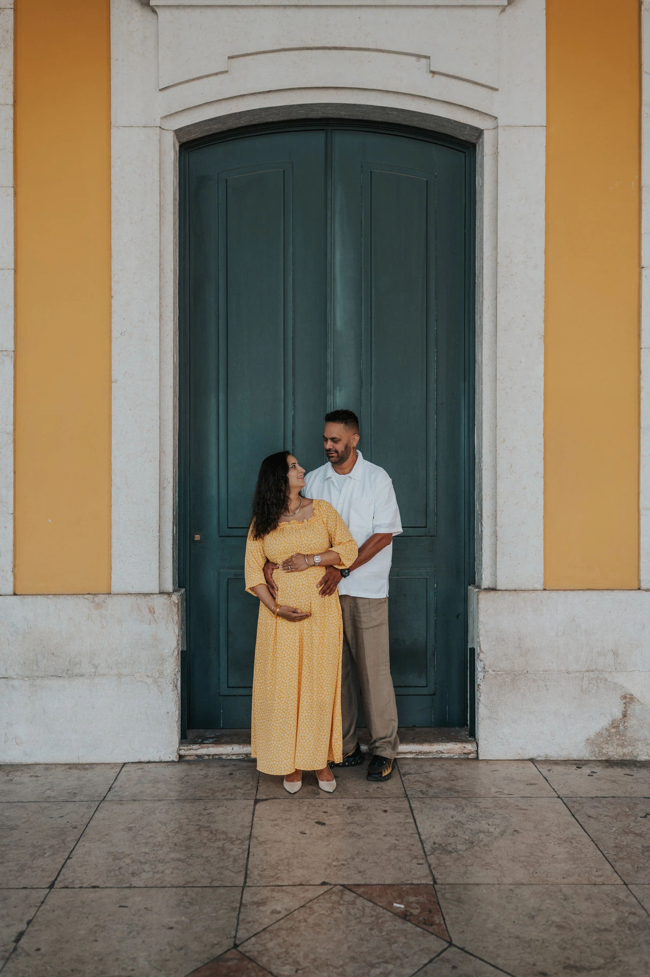The expectant parents standing together in an embrace beside the green door during their family and maternity photoshoot in Lisbon.