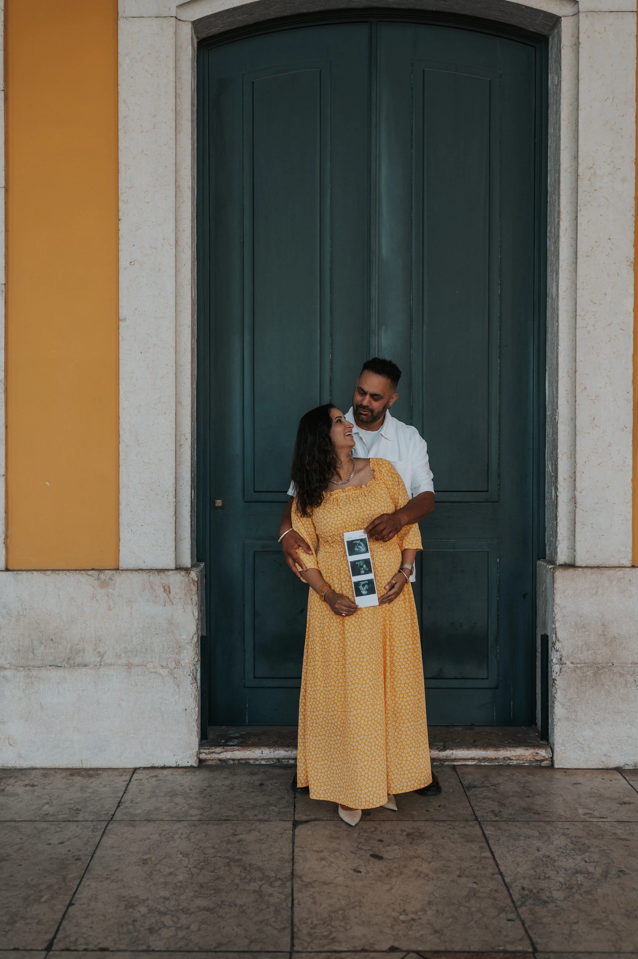 The expectant parents standing close together with the ultrasound photographs in the mother’s hands during their family and maternity photoshoot in Lisbon.