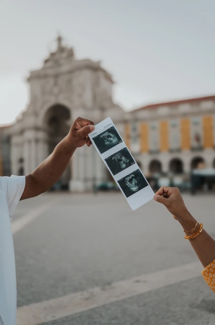Ultrasound prints with the square behind | Lisbon family and maternity photoshoot A strip of ultrasound photographs held up with Praça do Comércio’s arch in the background during their family and maternity photoshoot in Lisbon.