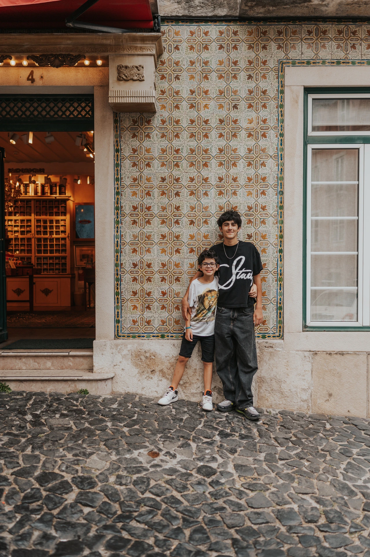 The two children standing together beside a colourful patterned tile wall during their family photoshoot in Lisbon.