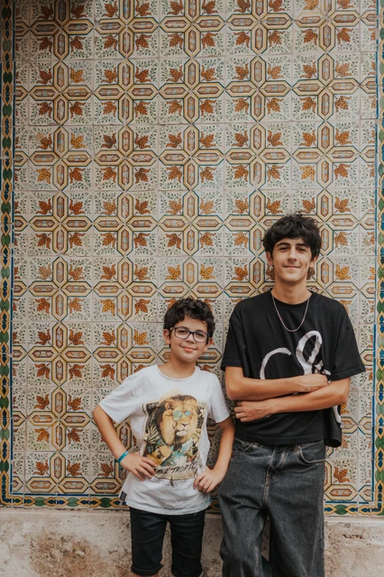 The two children standing together beside a colourful patterned tile wall during their family photoshoot in Lisbon.