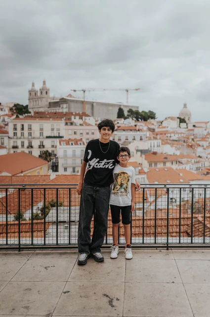 The children together above the city | Lisbon family photoshoot The two children standing together beside the viewpoint railing with Lisbon’s rooftops behind them during their family photoshoot in Lisbon.