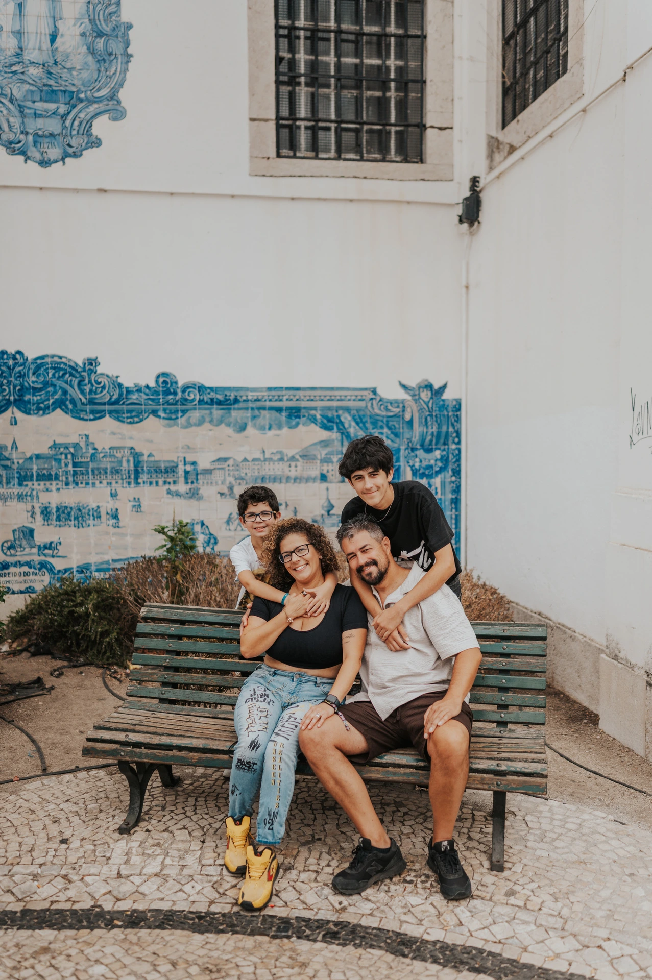 The family of four seated close together on a bench beside blue Portuguese tiles during their family photoshoot in Lisbon.