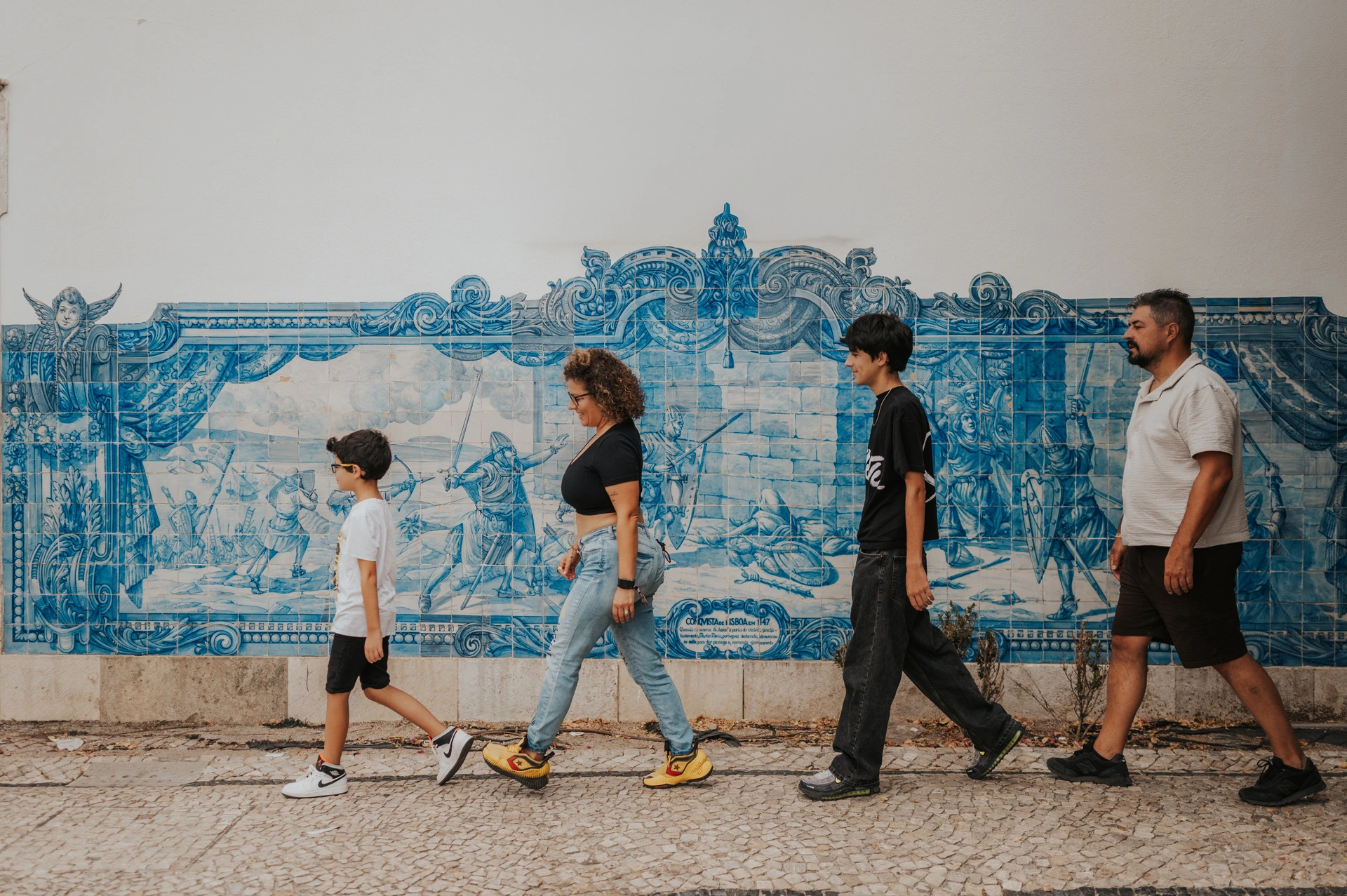 A family walk beside the blue tiles | Lisbon family photoshoot The family walking in a line beside a large blue Portuguese tile panel during their family photoshoot in Lisbon.