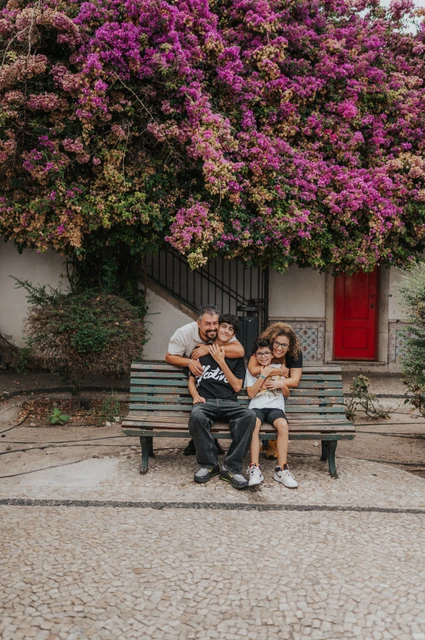 A family portrait beneath the flowers | Lisbon family photoshoot The family seated together on a bench beneath flowering branches during their family photoshoot in Lisbon.