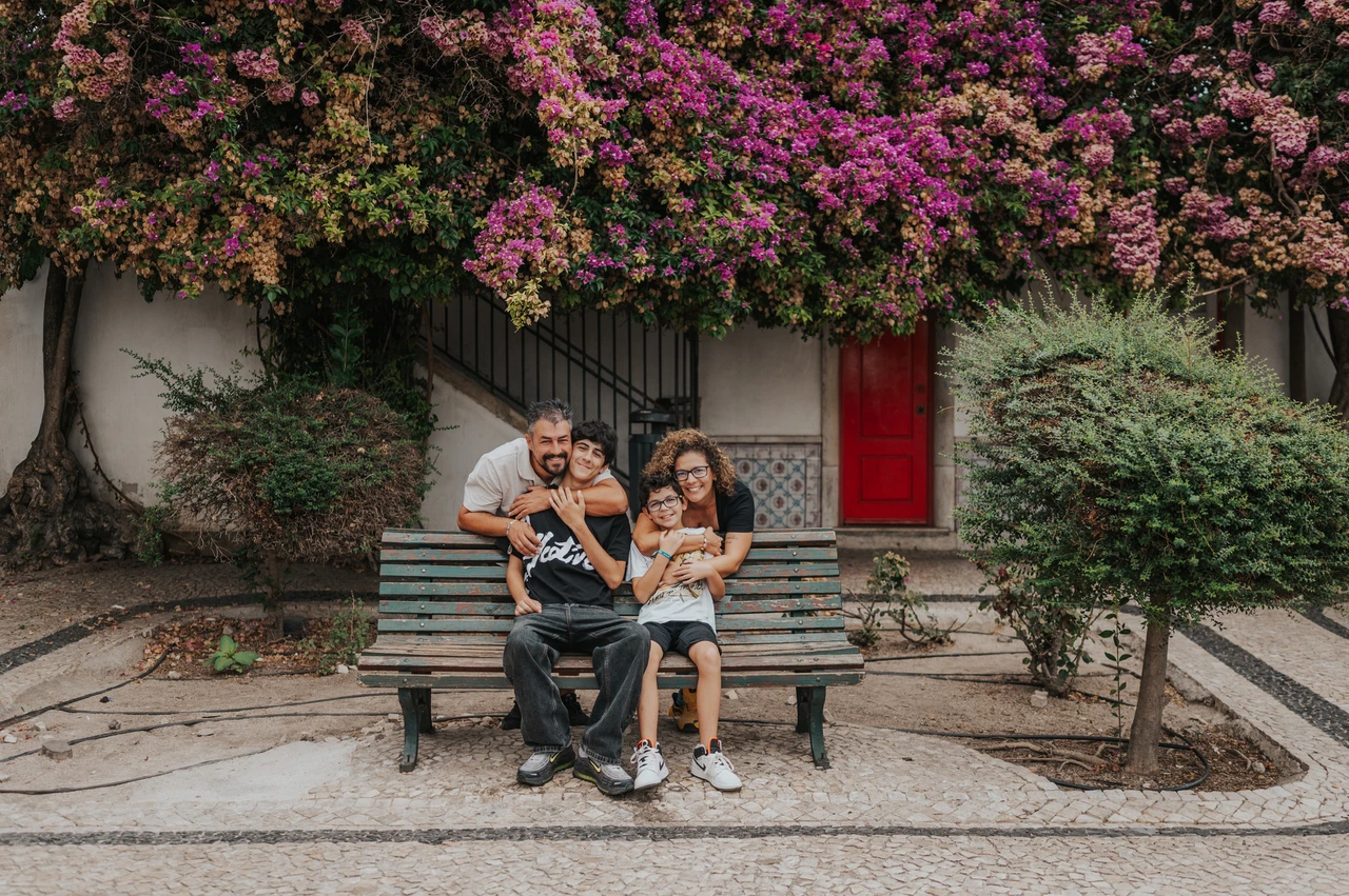A family portrait beneath the flowers | Lisbon family photoshoot The family seated together on a bench beneath flowering branches during their family photoshoot in Lisbon.