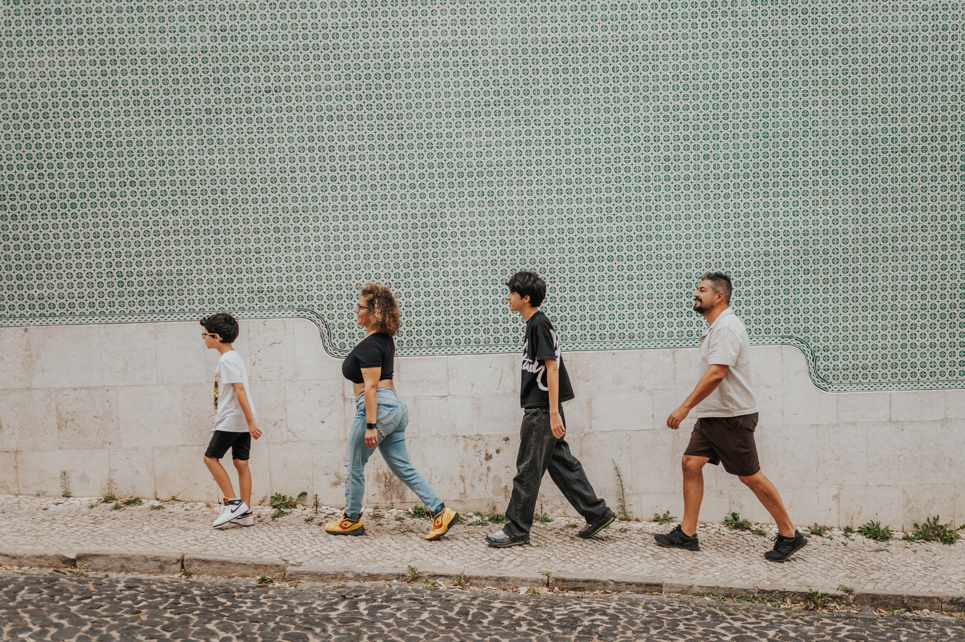 The family walking together beside the long green patterned tile wall during their family photoshoot in Lisbon.