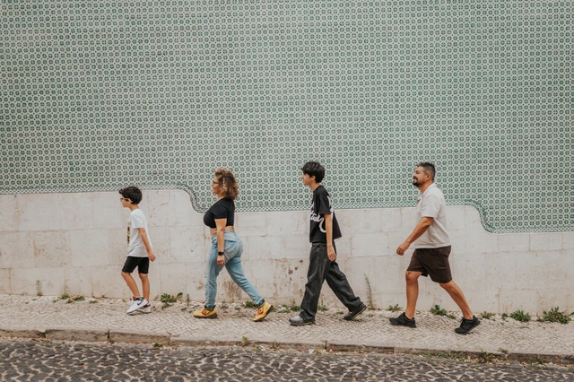 The family walking together beside the long green patterned tile wall during their family photoshoot in Lisbon.
