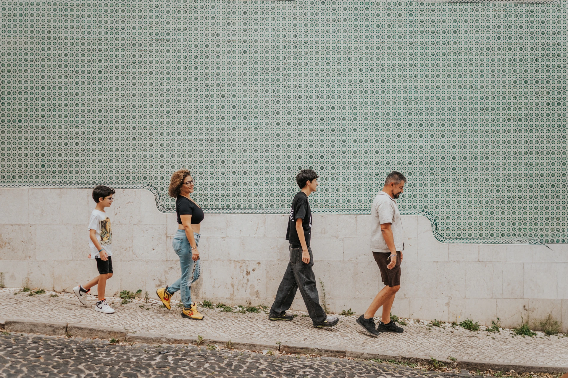 The family walking together beside the long green patterned tile wall during their family photoshoot in Lisbon.