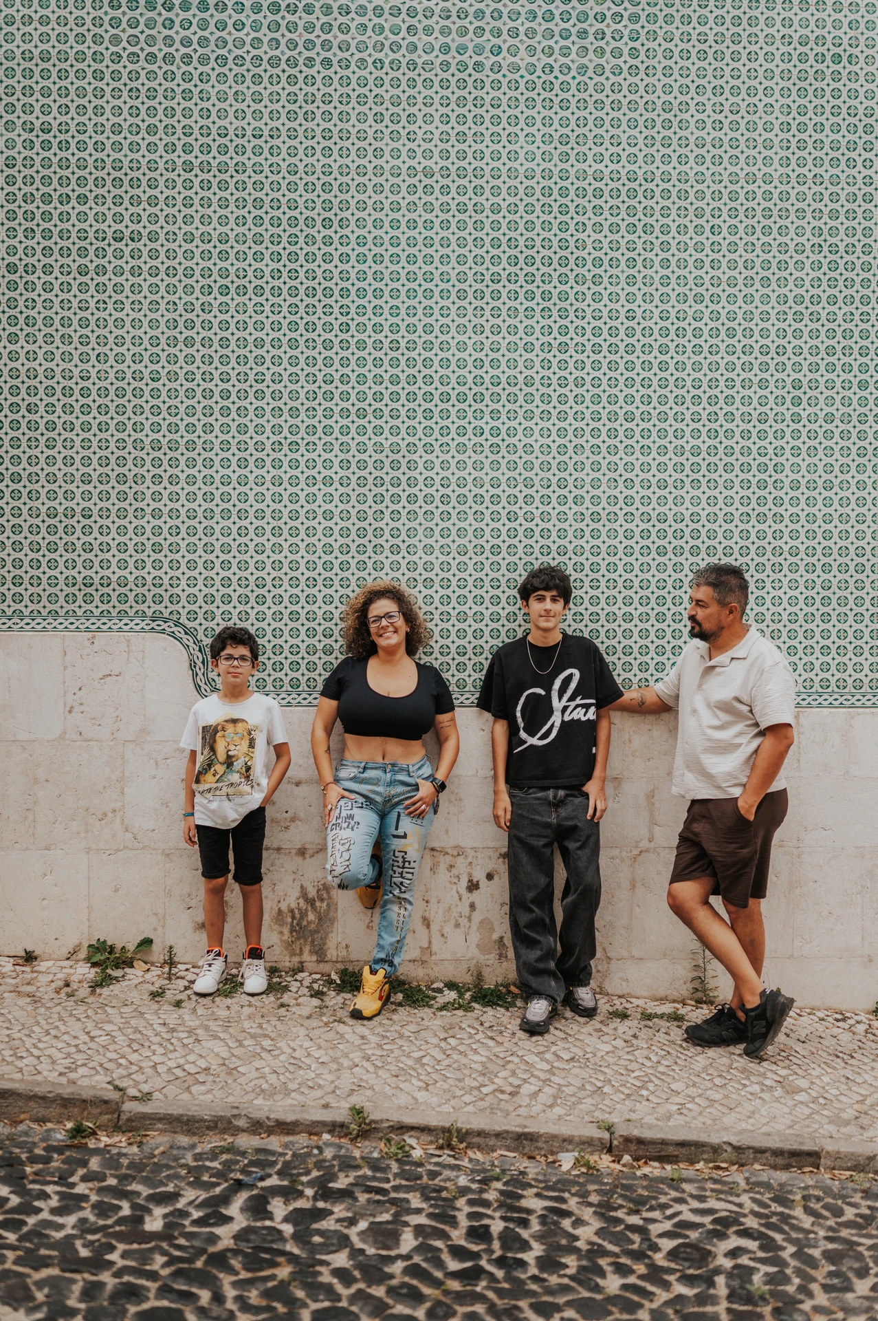 The family standing side by side along a green patterned tile wall during their family photoshoot in Lisbon.