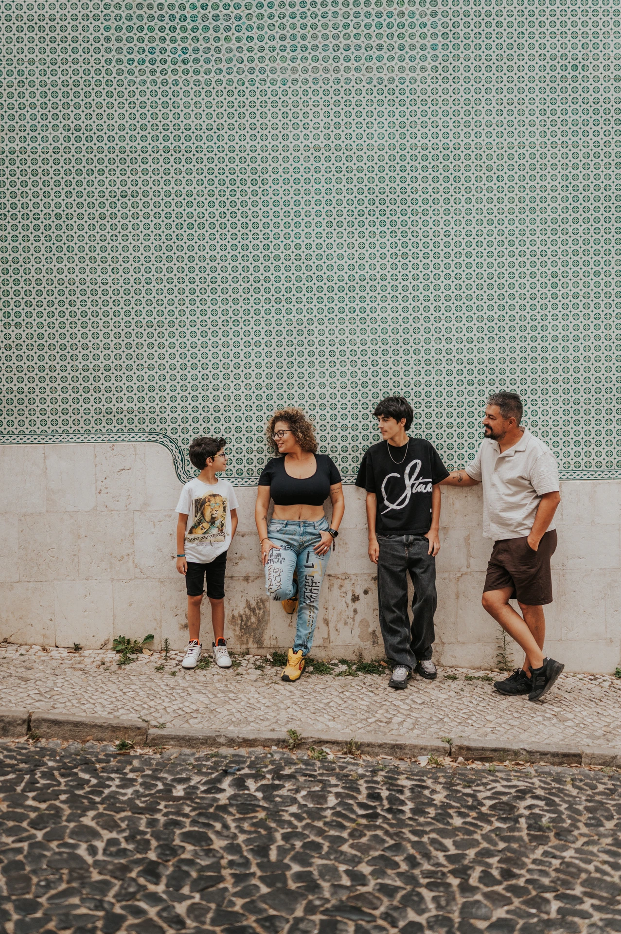 The family standing side by side along a green patterned tile wall during their family photoshoot in Lisbon.