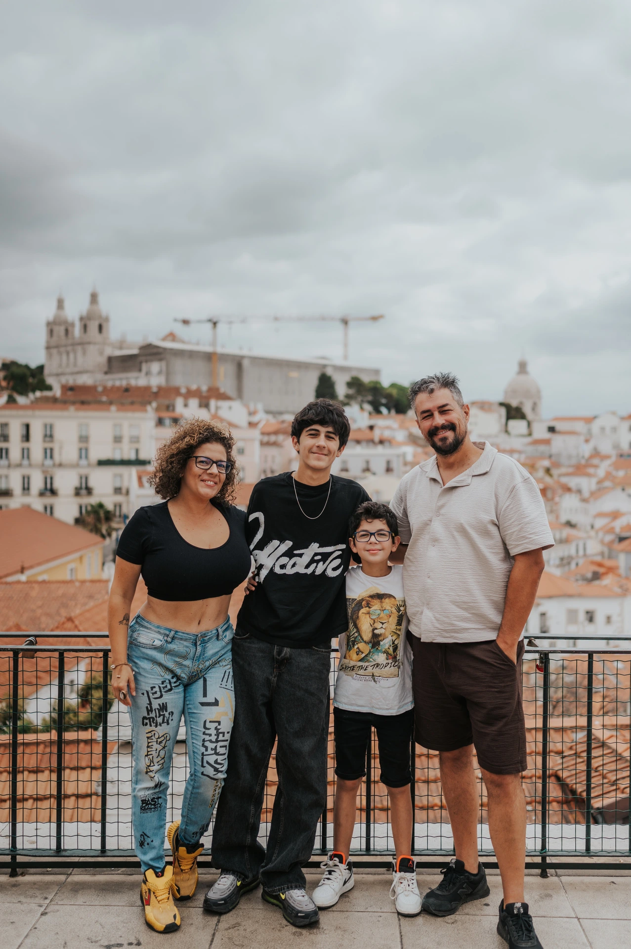 The family of four standing beside the viewpoint railing with Lisbon’s rooftops behind them during their family photoshoot in Lisbon.