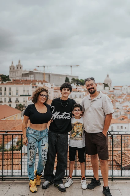 A family portrait above the rooftops | Lisbon family photoshoot The family of four standing beside the viewpoint railing with Lisbon’s rooftops behind them during their family photoshoot in Lisbon.