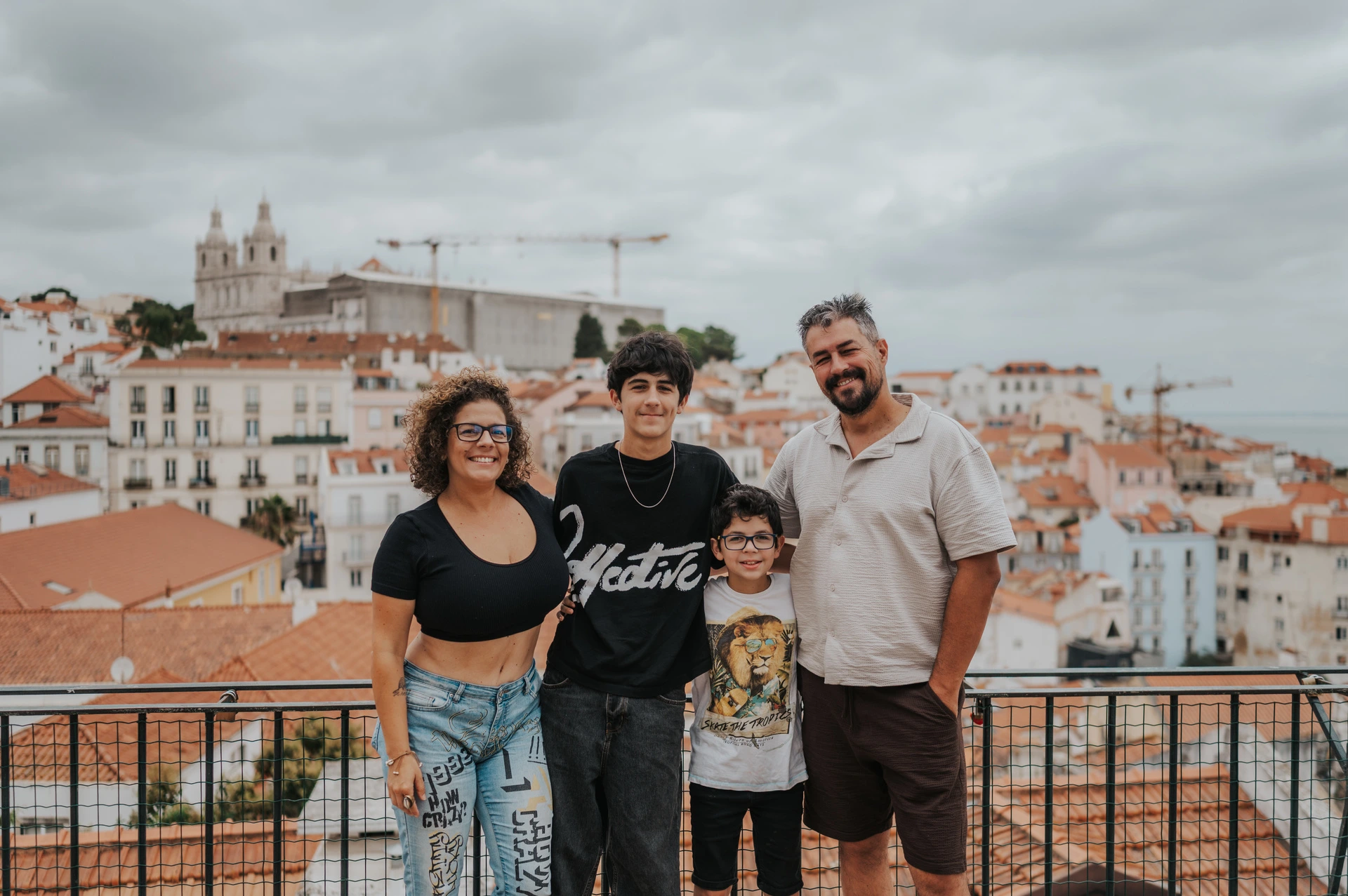The family of four standing beside the viewpoint railing with Lisbon’s rooftops behind them during their family photoshoot in Lisbon.