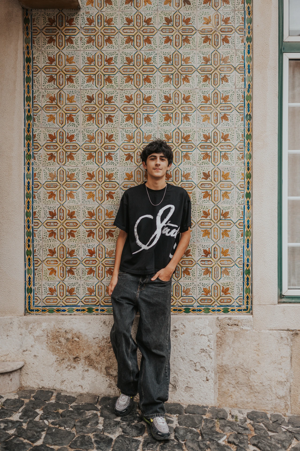 The older child standing beside the colourful patterned tile wall during their family photoshoot in Lisbon.