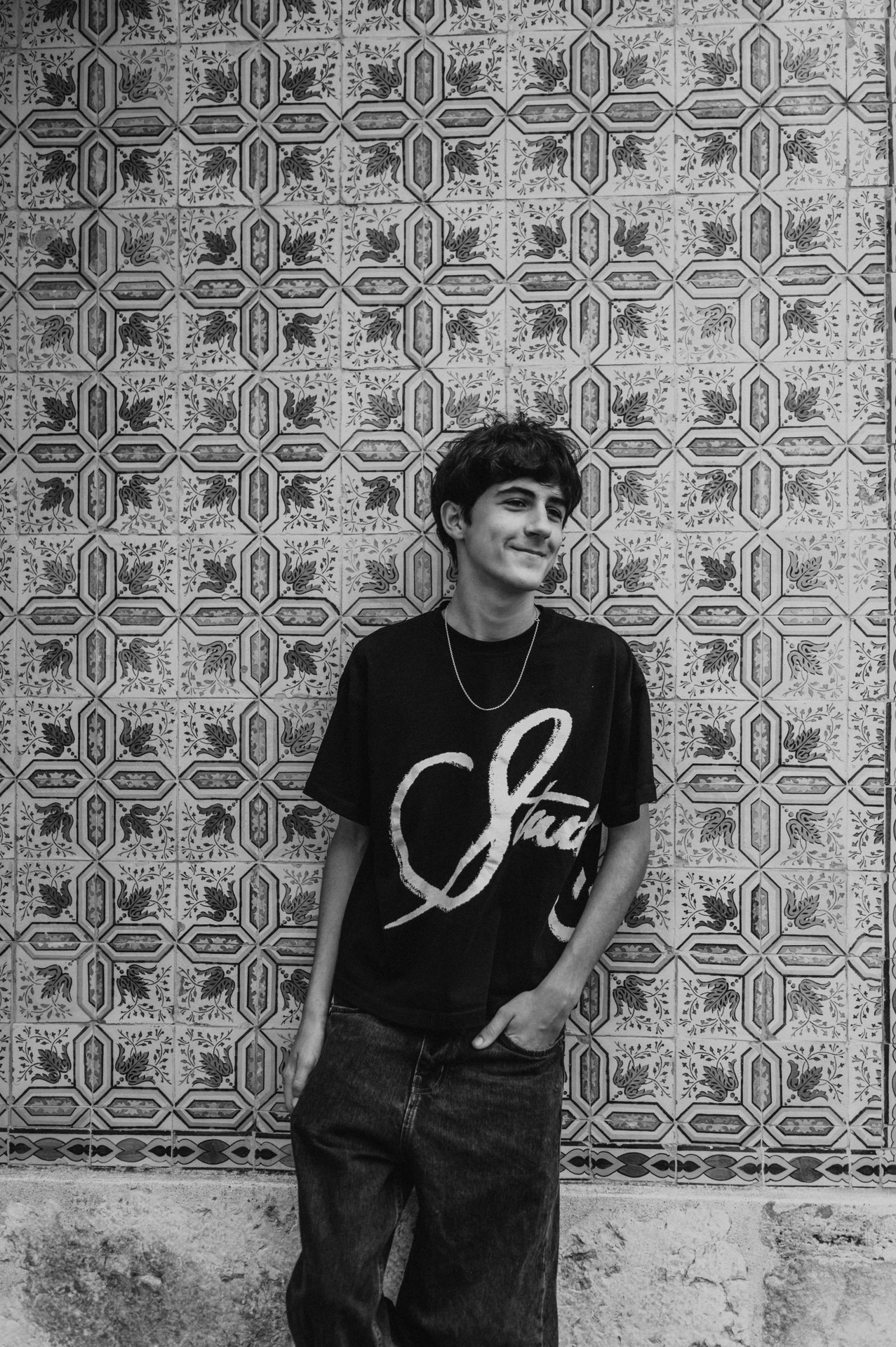 Black-and-white photograph: the older child standing beside the colourful patterned tile wall during their family photoshoot in Lisbon.