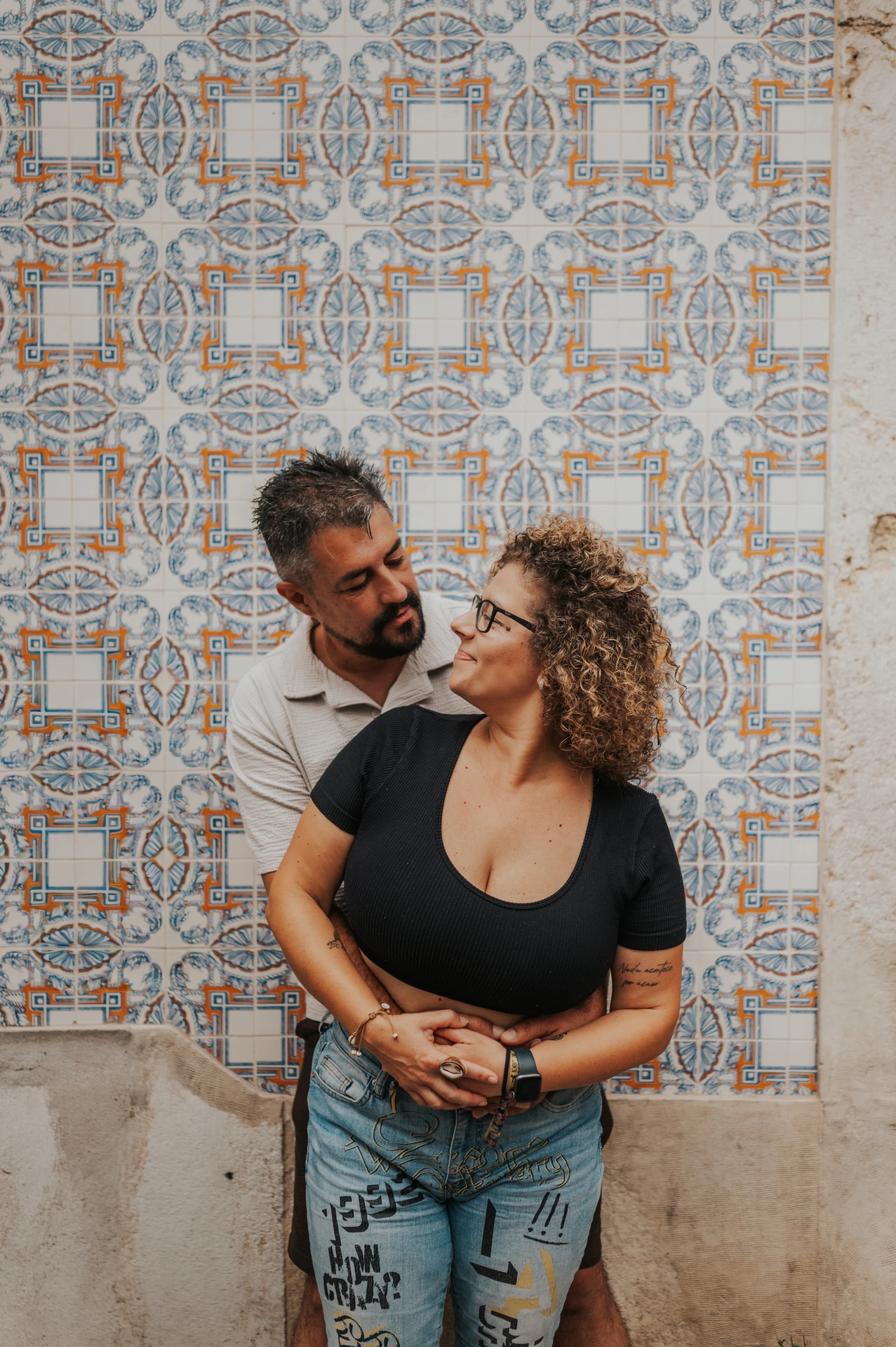 The parents embracing and looking at each other against a patterned tile wall during their family photoshoot in Lisbon.